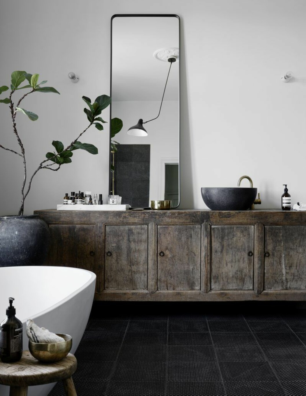 Badrum med dusch och badkar. Antikt kinesiskt skåp, spegel från Norm Architects för Menu, klinker och vask från Made a mano och produkter från Aesop i en marmorbricka från Hay, Lampa Lampe Matis BS4, växten är en fiolfikus.