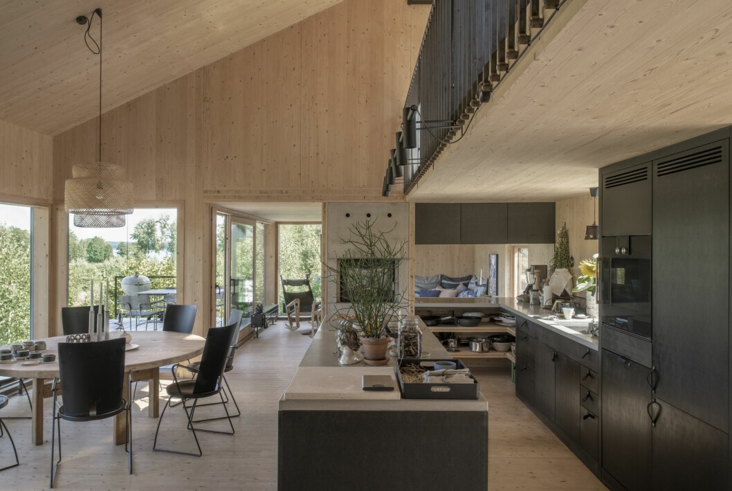 Köket är det självklara hjärtat i huset. Ina har sin drejskiva här och Johnny sitter en trappa upp i den öppna loftgången och ritar. Den öppna spisen har en vattenmantel som hjälper till med uppvärmningen av huset under kalla månader. Kök med öppen loftgång, öppen spis och matbord från Blocket.