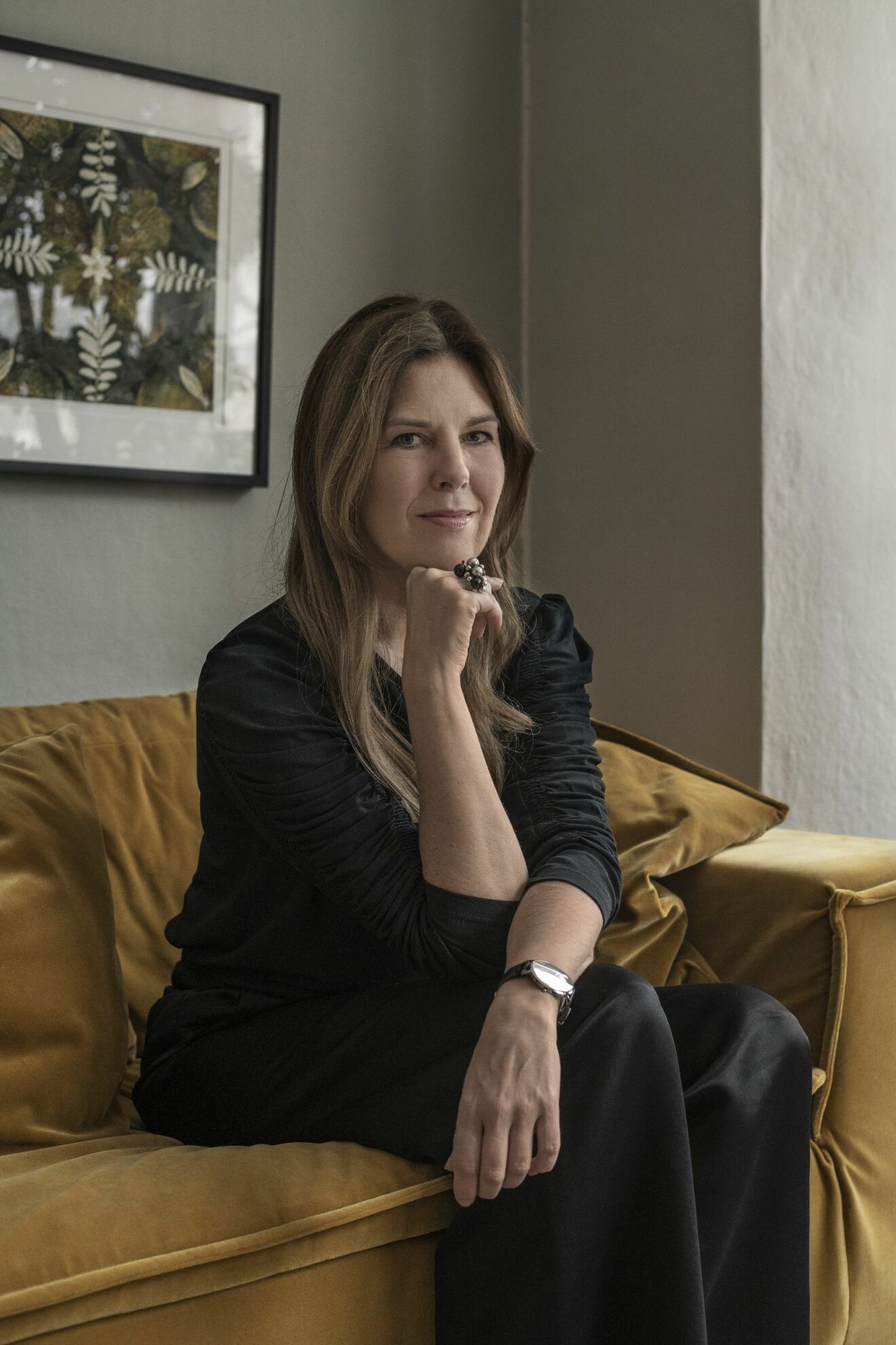 Karin Sköldberg i svart dress på den gula soffan i vardagsrummet.