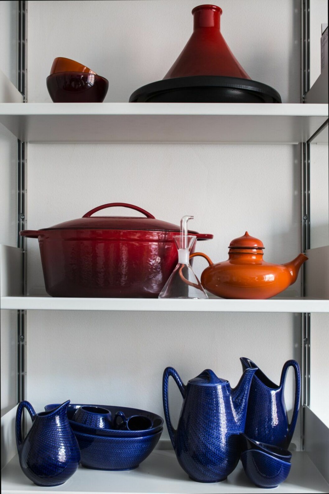 Färgstarkt i köket. Överst en tagine, kokkärl från Le Creuset. Mellanplanet en gjutjärnsgryta och Inger Perssons tekanna Pop för Rörstrand. Nedersta planet: Delar ur servisen Blå eld av Hertha Bengtson för Rörstrand. Hylla i köket