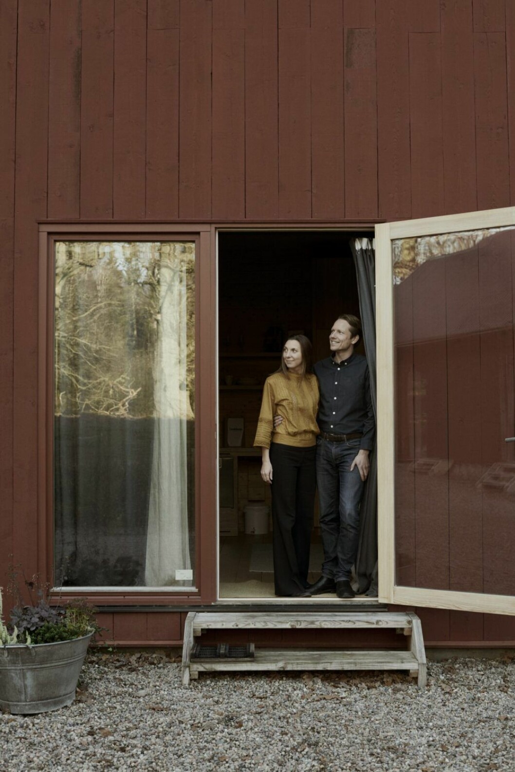 Julia och Carl Lindeborg har i sju års tid jobbat på sin livsdröm. Här står de i dörren till en av sviterna i Eco retreat-ladan som är målad i nedbrytbar Aurofärg från Tyskland. Kulören är Swedish red.