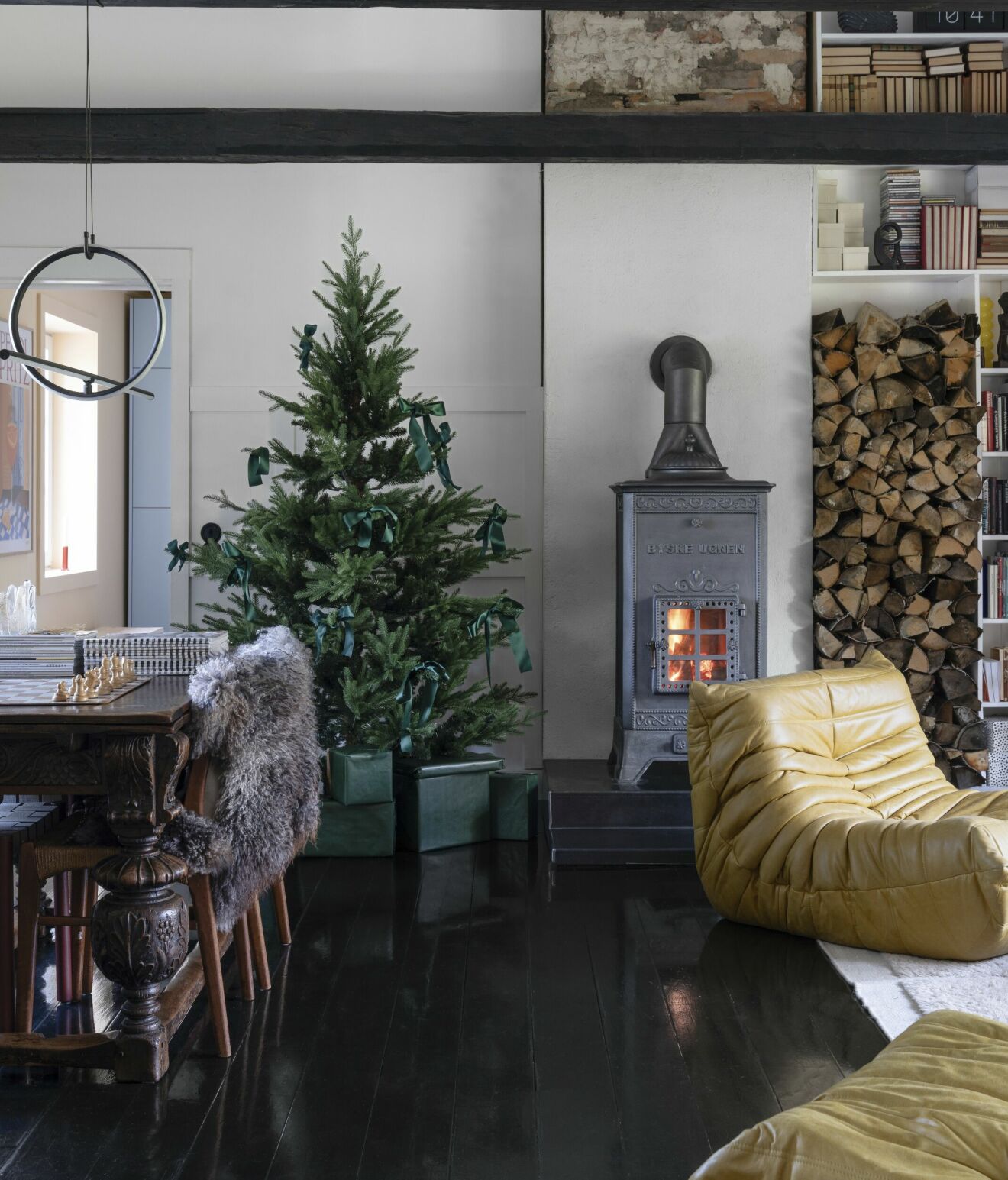 Julgran i vardagsrum. Gjutjärnsugnen från Byskeugnen, bord i ­ny­barockstil, svart golv med färg från Trestjerner.
