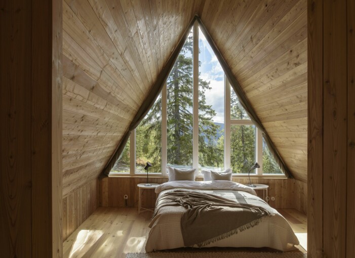 Master bedroom på övervåningen. Här framträder A-frame-typologin i sin allra renaste form. En uppglasad gavel med spröjsade fönster klättrar hela vägen upp till nock. Lampor från engelska Anglepoise, nattduksbord från Ikea. De trekantiga rullgardinerna är specialsydda. Master bedroom i A-frame-hus.