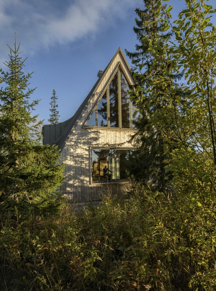 Anders Smedberg sedd genom västfasaden, på väg ut på terrassen. Tids nog kommer den värmebehandlade furupanelen från Kebony att bli lika grå som takplåten. A-frame-huset från sidan.