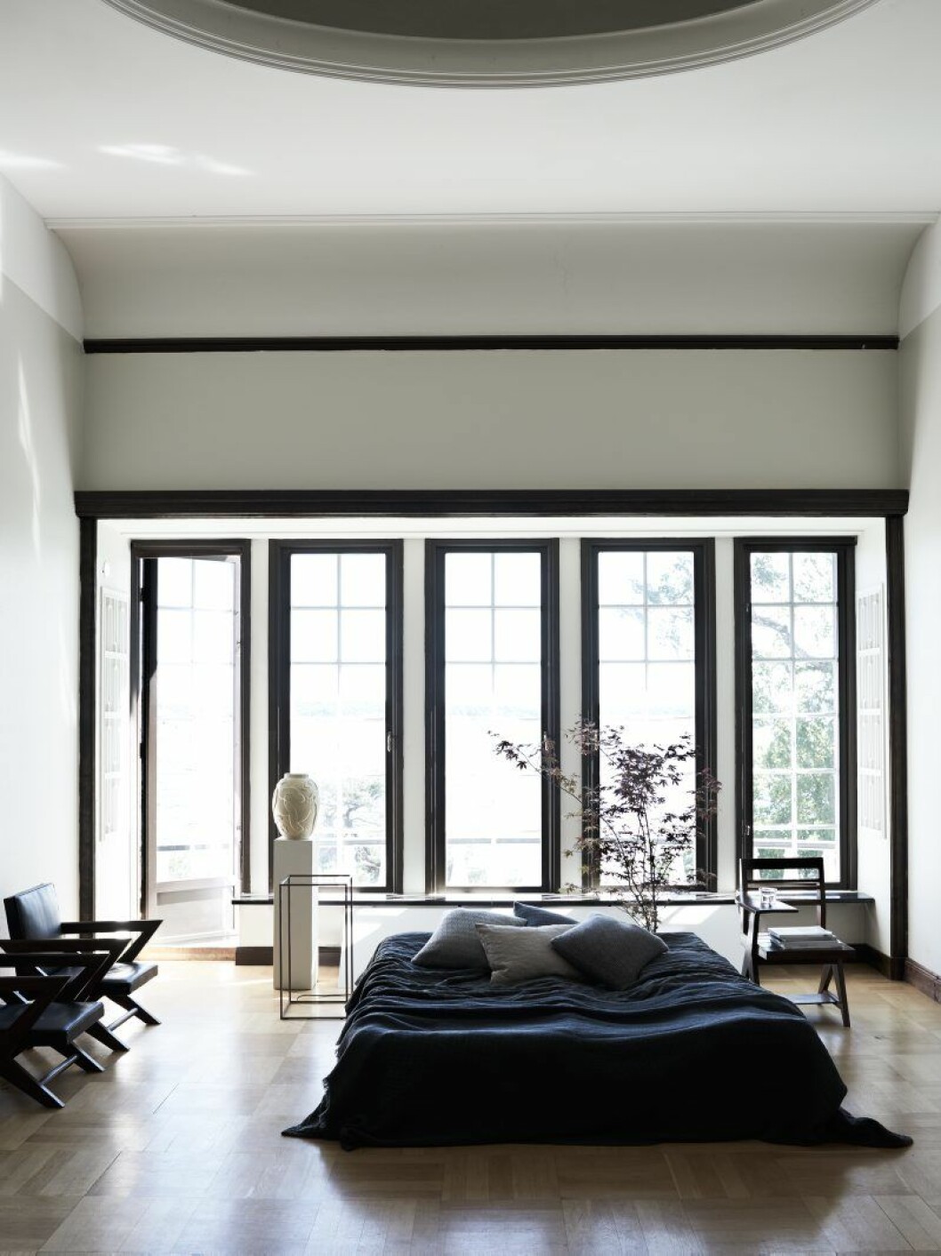 Svarta läderstolar och sängbord (stol med bricka) av Pierre Jeanneret från Galerie maison première. Piedestal av Matti Carlson, på den vas från Dusty deco, lampa Ipnos, Flos, sängkläder och kuddar, Society. Träd i bakgrunden, Christoffers blommor.