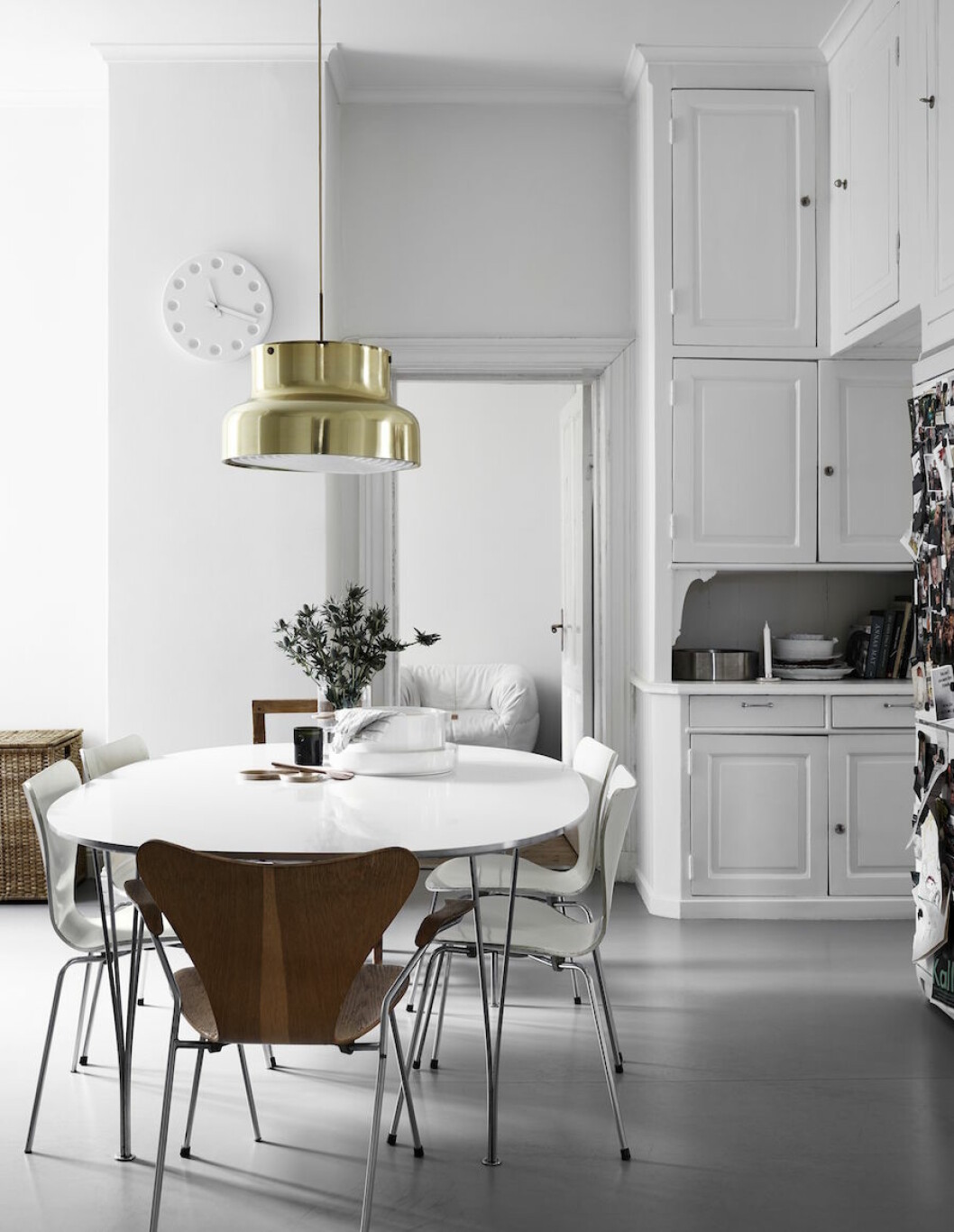 <em>I köket står ett ellipsbord i centrum, omringat av </em>Arne Jacobsens Sjuan-stolar. Ovanför dinglar en Bumling i mässing. På bordet keramik av Carina Seth Andersson för Arket.<em> </em> Bild på Anna Teurnells kök, taklampa i mässing och vitt matbord.