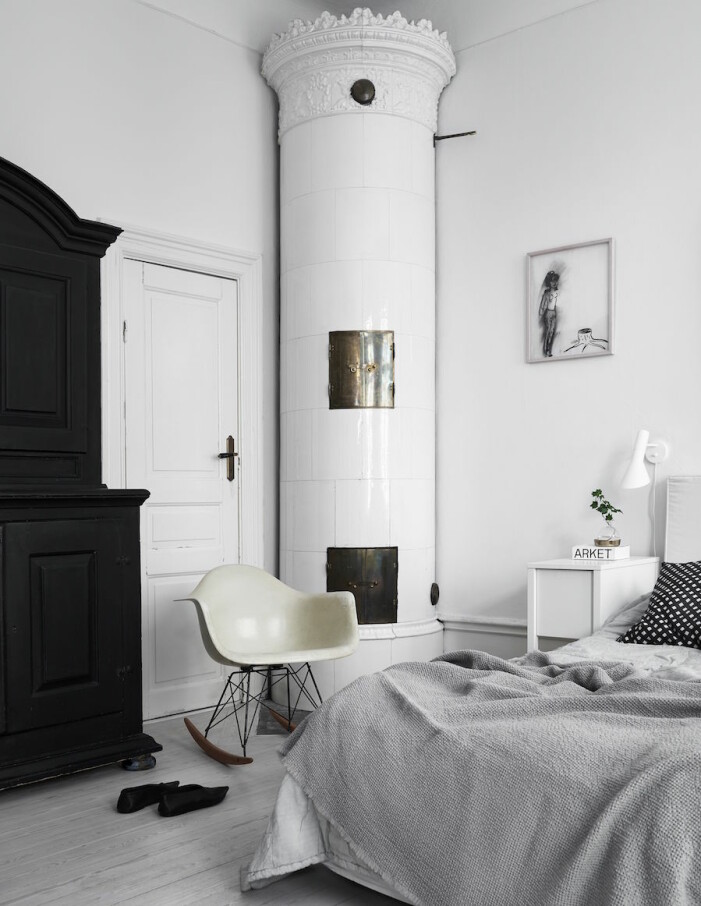 <em>Eames gungstol</em> gungstol i sovrummet. Läslampa av Arne Jacobsen. Det svarta skåpet kommer från Annas familj. Konst av Helene Billgren. »Vi har alltid haft svarta skåp, min mamma, min mormor och jag, det hör liksom till.« <em> </em> Bild på Anna Teurnells sovrum med kakelugn.