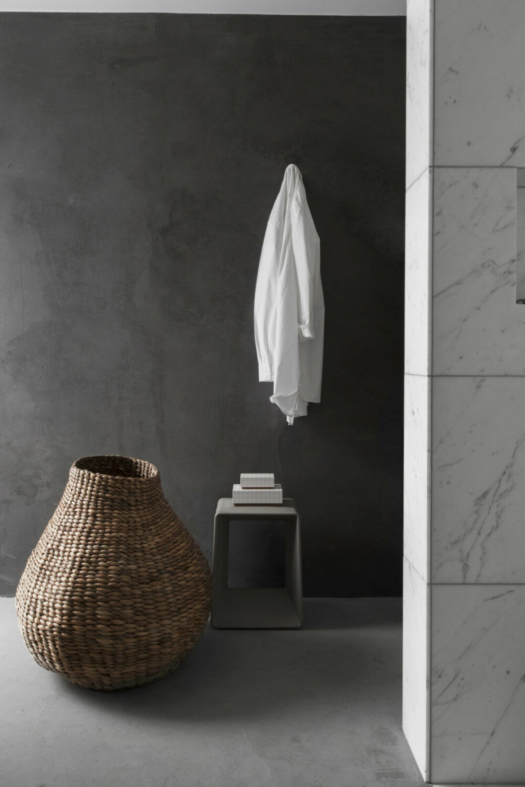 Den svartfärgade betongväggen skiljer badrummet från sovrummet.Till höger: Korg från Muubs och pall Air low, design Héctor Serrano för Gandiablasco. Stilleben hemma hos Asplund.