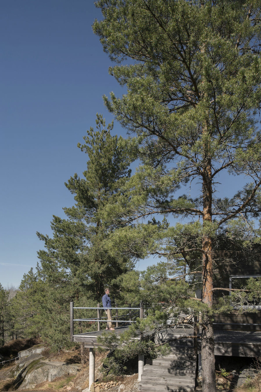Det stora trädäcket vetter åt skogen, och till Johans förtjusning är det stenigt och klippigt – vilket innebär att man slipper klippa gräset. Bild på Johan Fredlund ute på trädäcket på lantstället vid Ingarö i skärgården.