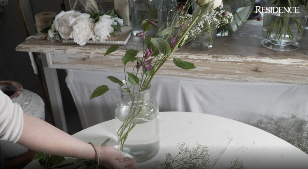 Sandra visar blommorna i vasen och poängterar den höga vattennivån. En bukett behöver mycket vatten. Blommor i vas.