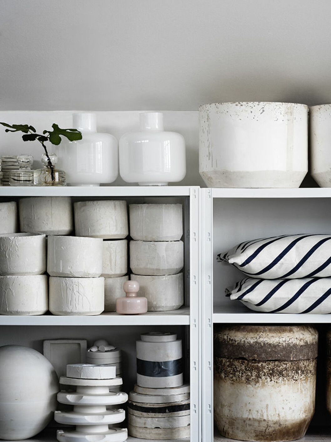 På hyllan i ateljén bland gipsformar och annat arbetsmaterial. Vaser <em>Flower</em> i klarglas och <em>Ming</em> i vitt underfångsglas, samt <em>Flower</em> i rosa. Blåsta i grafitformar i Thailand. ”Det finns en liten skevhet i dem, där syns hantverket.” Mönster <em>Mint</em> på kuddfodral. Carina Seth Andersson Marimekko Foto Pia Ulin1