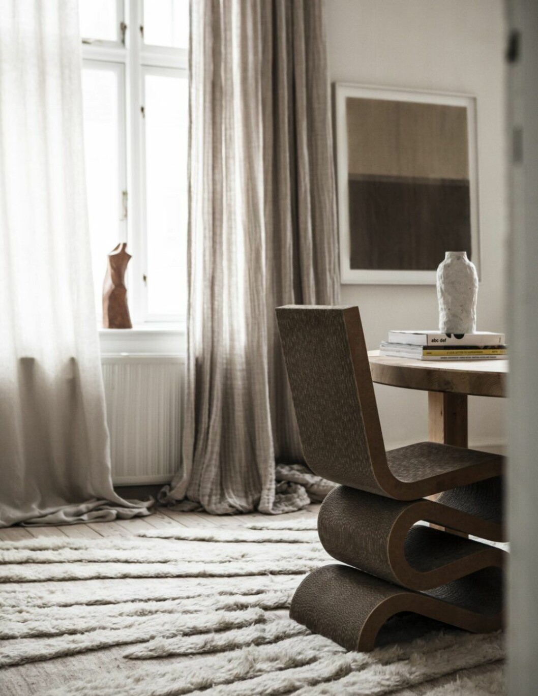 Den ikoniska Wiggle chair av arkitekten Frank Gehry (Vitra), första gången byggd i all hast av kartonger inför ett Nasa-möte 1969. Tavla av Åsa Stenerhag. Skulptur, okänd konstnär, inropad på auktion. Gardiner från Astrid. Mattan är Cappelen dimyrs mjuka bjässe.