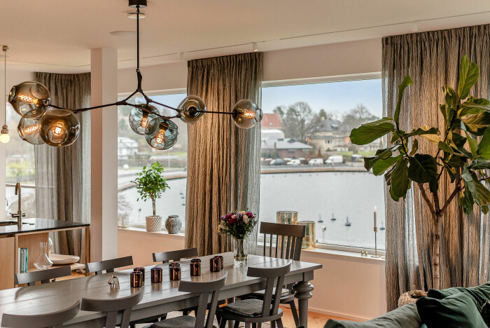 Stort matbord med plats för många i det ljusa och öppna köket med matplats. Utanför syns Värtan. Kök i villa som är till salu i Djursholm