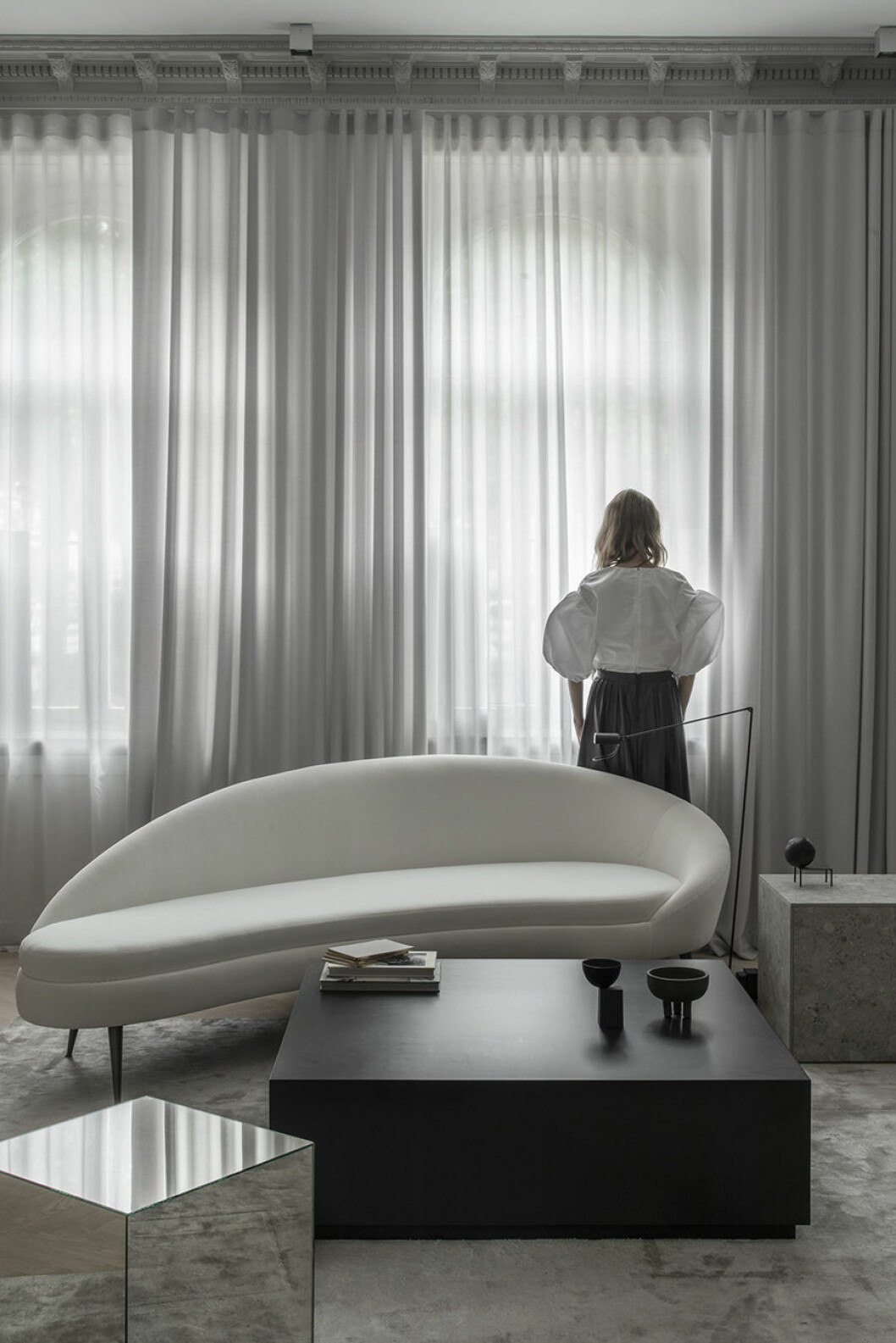 Gardinerna i tunn ull sitter på en Wave-skena för att få ett snyggt fall, och är gjorda hos textilproducenten Astrid i Stockholm. Matta Solid Viscose i färgen Francis Pearl, från Layered. På bordet står en liten skål på tre ben i keramik från Copenhagen 101, och en liten svart figur som blev över från en av Emmas stylingjobb. På Emmas sidobor från Apartment Stories finns en liten skulptur med klot av skulptören Ingemar Svensson, en bröllopspresent. emma b mot fönster