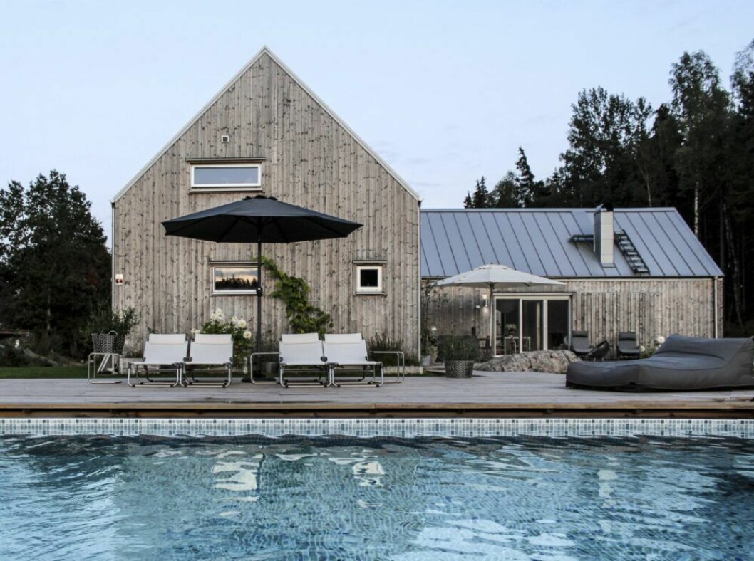Huset är ritat av arkitekten Gunnar Bäckman och byggt i ladustil. När fönsterluckorna stängs ser det ut precis som en lada. <span class="s1">Vid poolen står solsängar och sidobord från Fiam. Parasollet i bakgrunden kommer från Newport.</span> Poolvy Karin Boo Wiklander