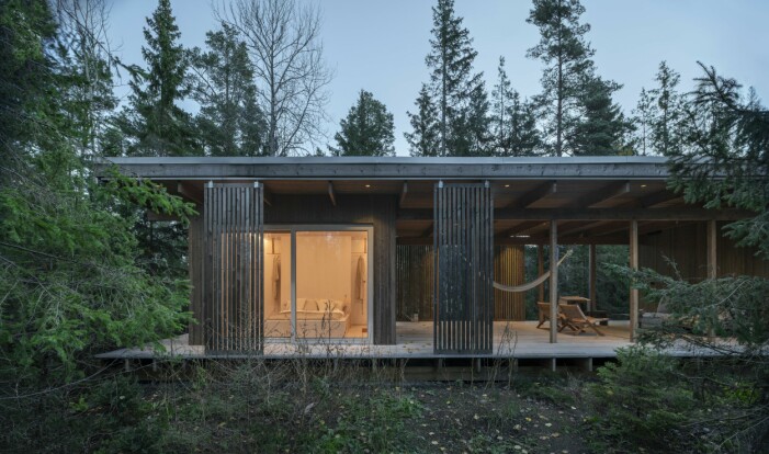 Huset i skogen svävar lätt ovanför marken, varsamt placerat i den vilda växtligheten. Arkitektritad fritidsvilla.