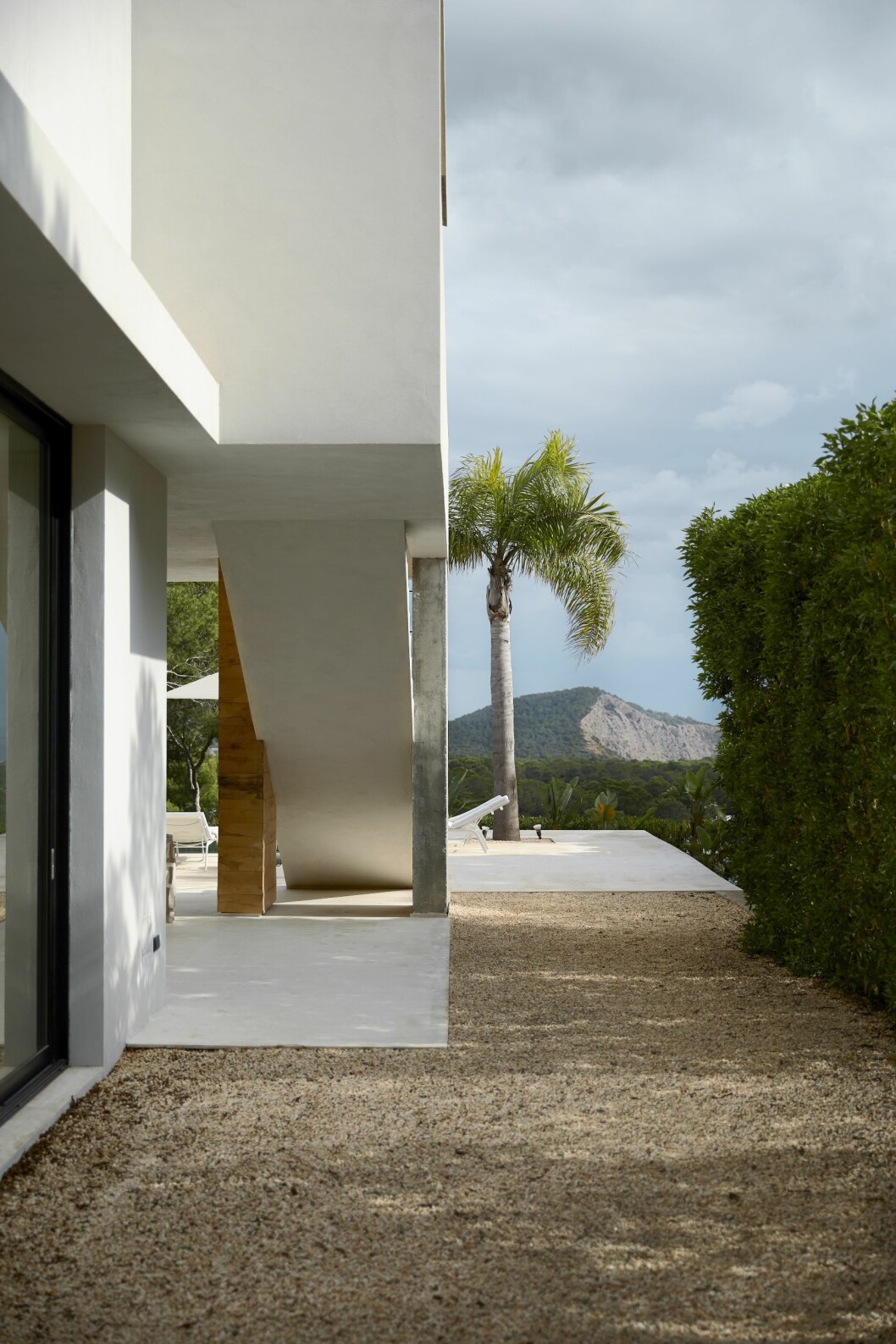 En stilstudie vid husets kortsida, kalkstensgrus mot vit puts och en vacker palm som bildar en siluett mot havet som ligger precis nedanför tomten. Vacker vy hemma hos Charlotte Gyllenhammar på Ibiza.