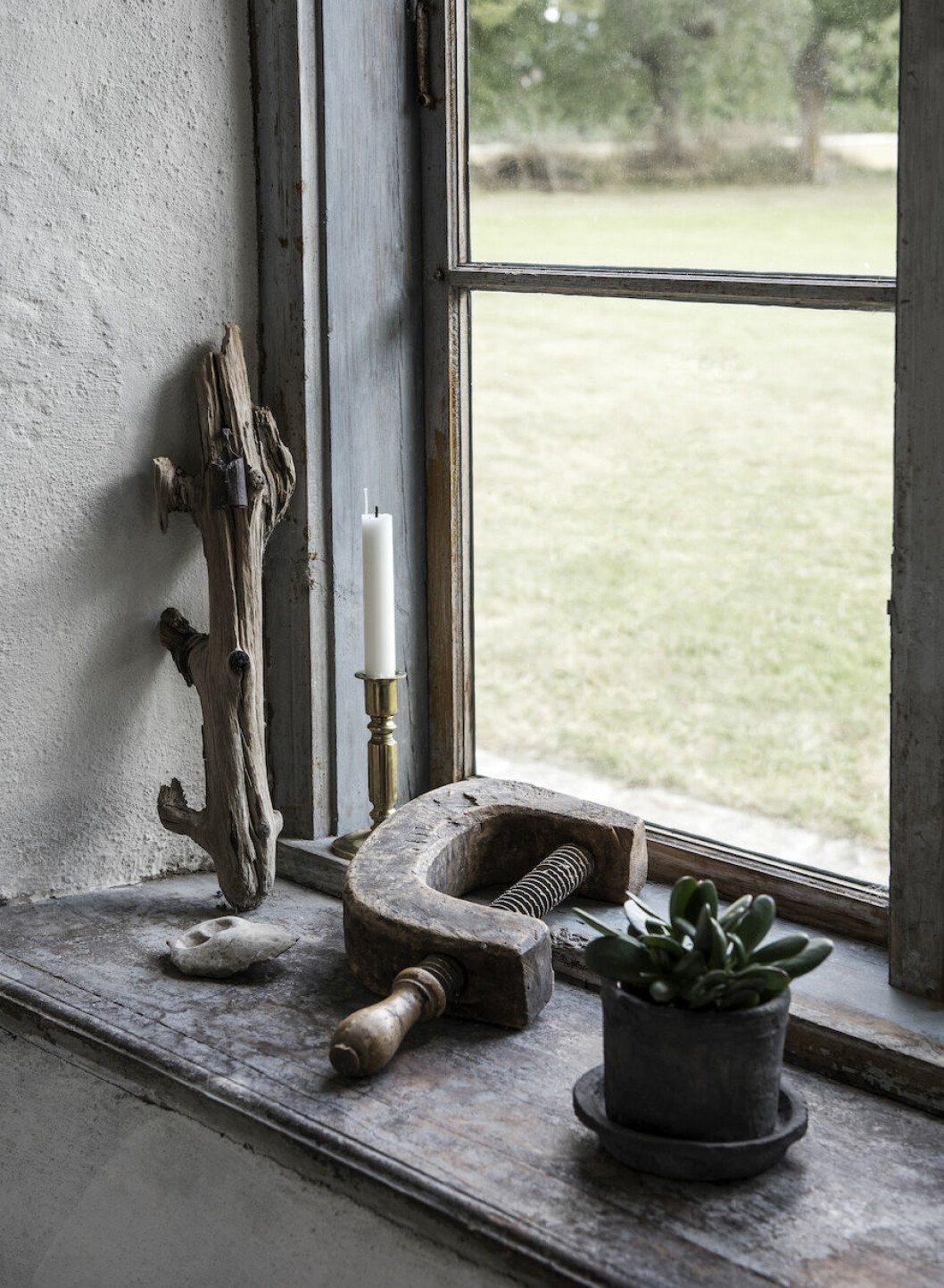 De djupa fönsternischerna ger ett härligt ljus i huset. En antik tving i trä får agera prydnad på fönsterbänken. Antik tving och växter hemma hos Johan Lindskog och Joanna Sundström.