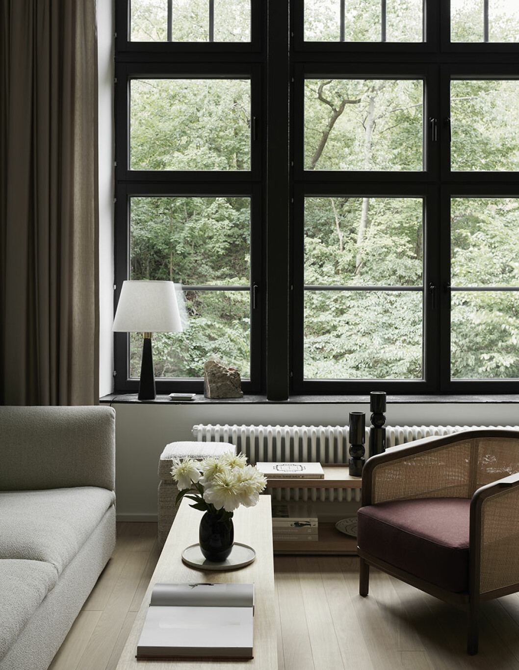 Växtligheten bildar ett konstverk utanför fönstren. Sidengardiner <em>Aruba</em>, Astrid textiler. Bord <em>BIT sidetable</em> i ek, Massproductions. Soffa <em>Retreat</em>, Fogia. Fat, Mateus. Lampa designad av finländska formgivaren Lisa Johansson-Pape. Bokstöd i sten, Nordiska galleriet. Sittpall <em>Louise, evolution 21</em>, Bert Van Hoecke interiors. Ljusstakar i svart marmor, Lee Broom. Fåtölj <em>Mozart</em>, design Centro studi flexform, Nordiska galleriet. Sideboard i ek och metall, Vincent Van Duysen. hans hjelmqvist relations