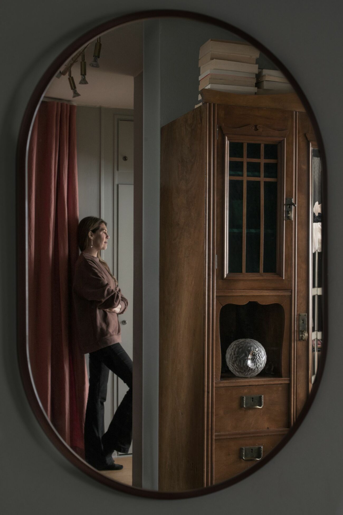 I en oval spegeln från Montana syns Karin Sköldberg stå lutad mot väggen. Vi ser hennes morfars skåp och ett draperi från Astrid.