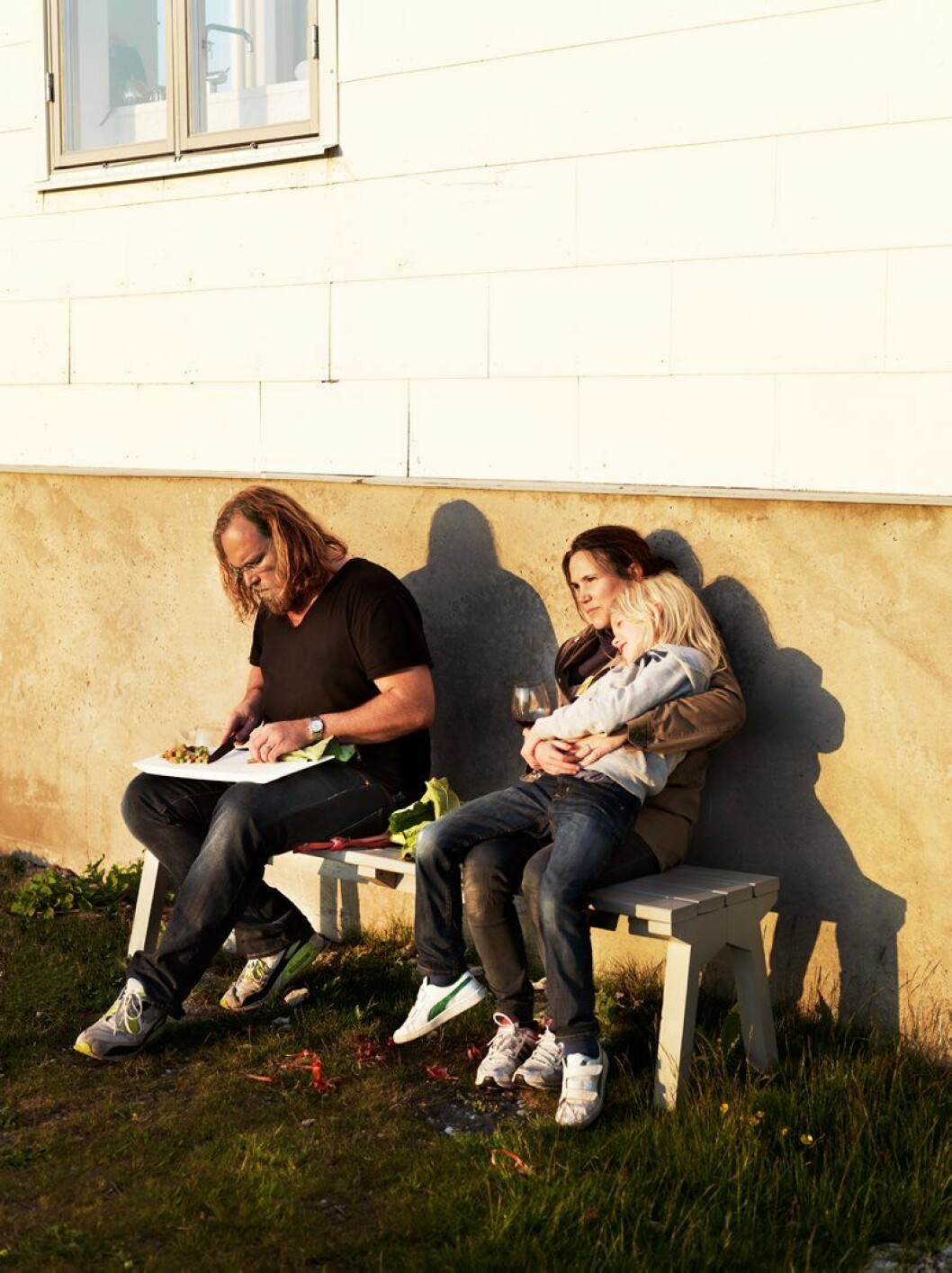 Mårten, Jessica och Okee Knutsson bänkade i solnedgången. Bänken är en protoyp ritad av Jessica Signell Knutsson. Hemma hos Jessica Signell