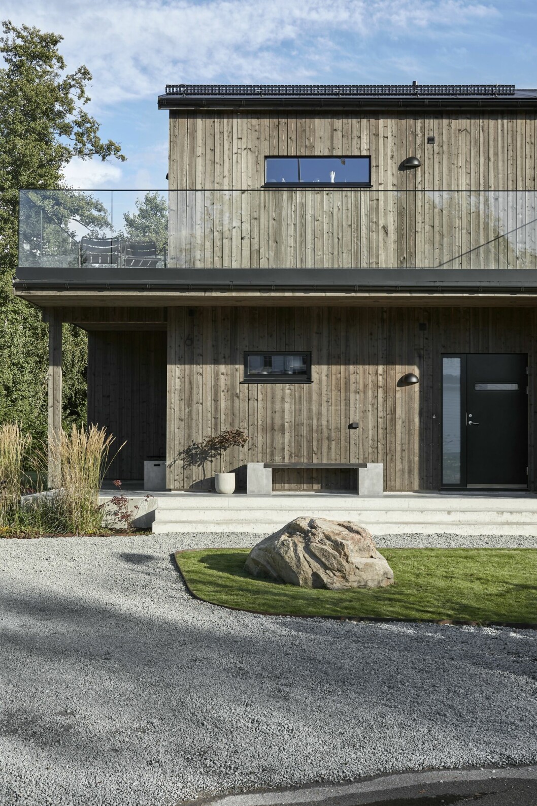 Några få fönstergluggar bryter de stående brädornas linjespel på fasaden mot gatan, men inga fönsterfoder eller andra dekorationer bryter av. Hemma hos MK Design Studios grundare balkong