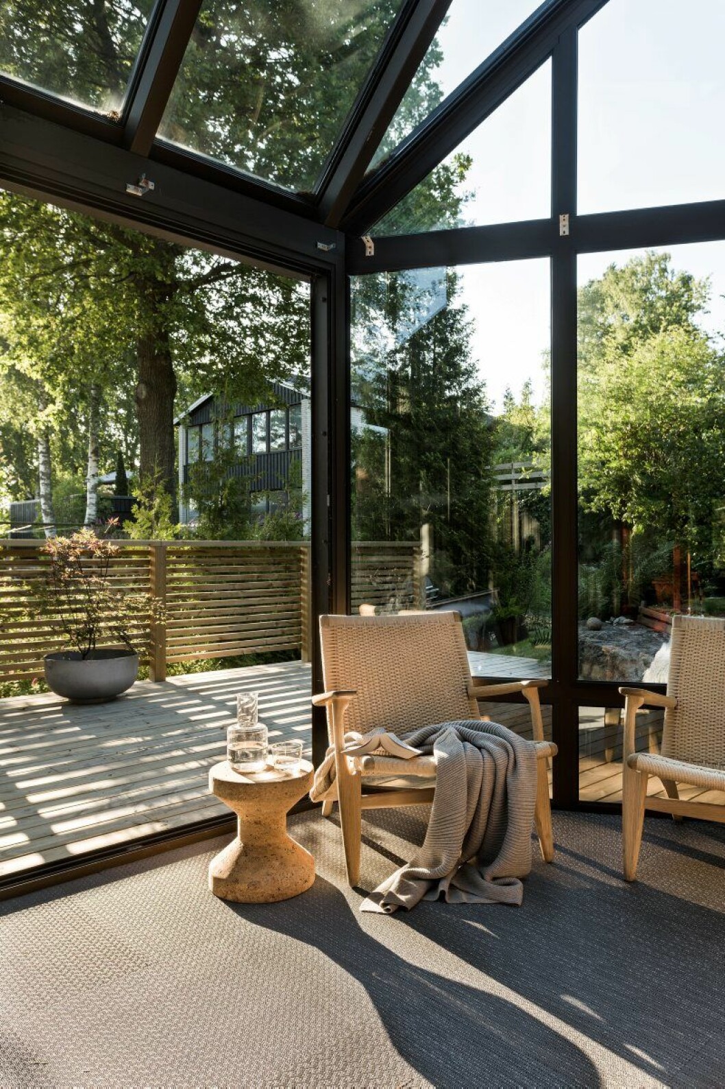 Det inglasade uterummet med dubbel takhöjd sträcker sig en våning upp till en annan inglasad uteplats. Golvmattan heter Artisan slate och kommer från Bolon, pall av Jasper Morrison från Vitra, stolar CH-25 av Hans J Wegner, Nordiska galleriet. På terrassen skymtar en kruka från Friends & founders. inglasat uterum