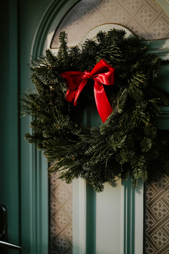 Enkelt i grönt och rött eller med fina dekorationer? Hitta din egen stil när du gör DIY-kransen. Foto: Phil Hearing/Unsplash klassisk julkrans med granris och röd rosett
