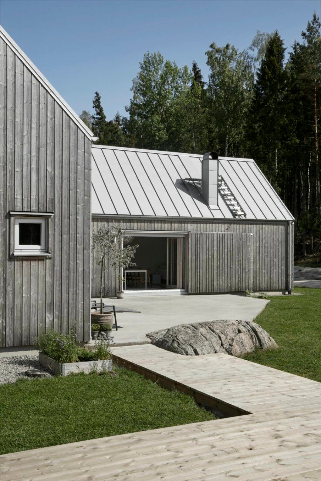 Trädäcket förlängs med en gång av trä som likt en brygga leder ut i trädgården. I panelen finns en stor skjutdörr som gömmer öppningen mellan det stora rummet och uteplatsen utanför. Trädäck hemma hos Karin Boo Wiklander