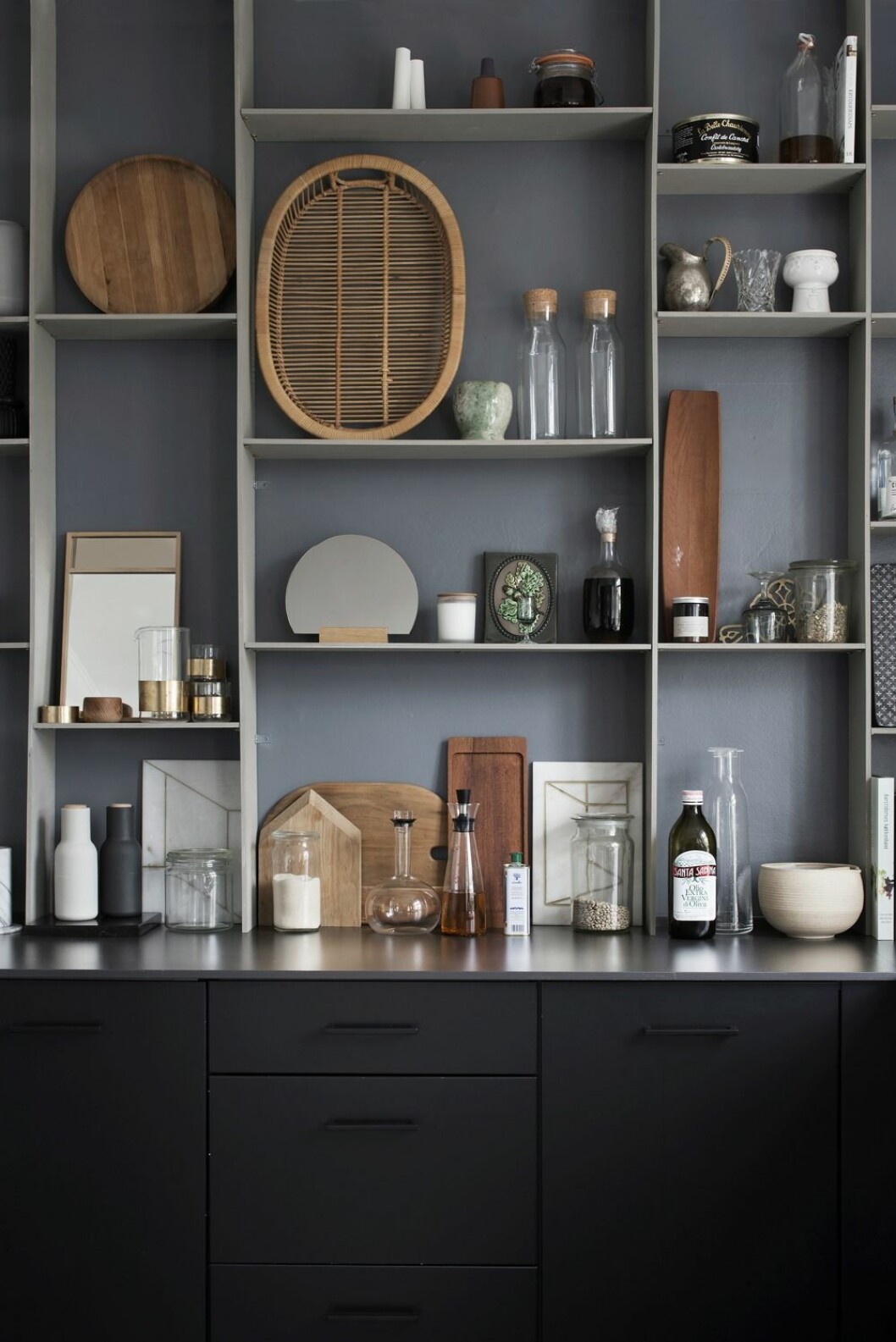 Gråskala. Ena köksväggen täcks av en egentillverkad hylla fylld med arvegods och egen design. Den stora rottingbrickan har Kristina fått ta över från sin mormor. Spegel Halfmoon, bricka Mirror tray och underlägg/ dekoration, Marble perspective, alla från Kristina Dam Studio.