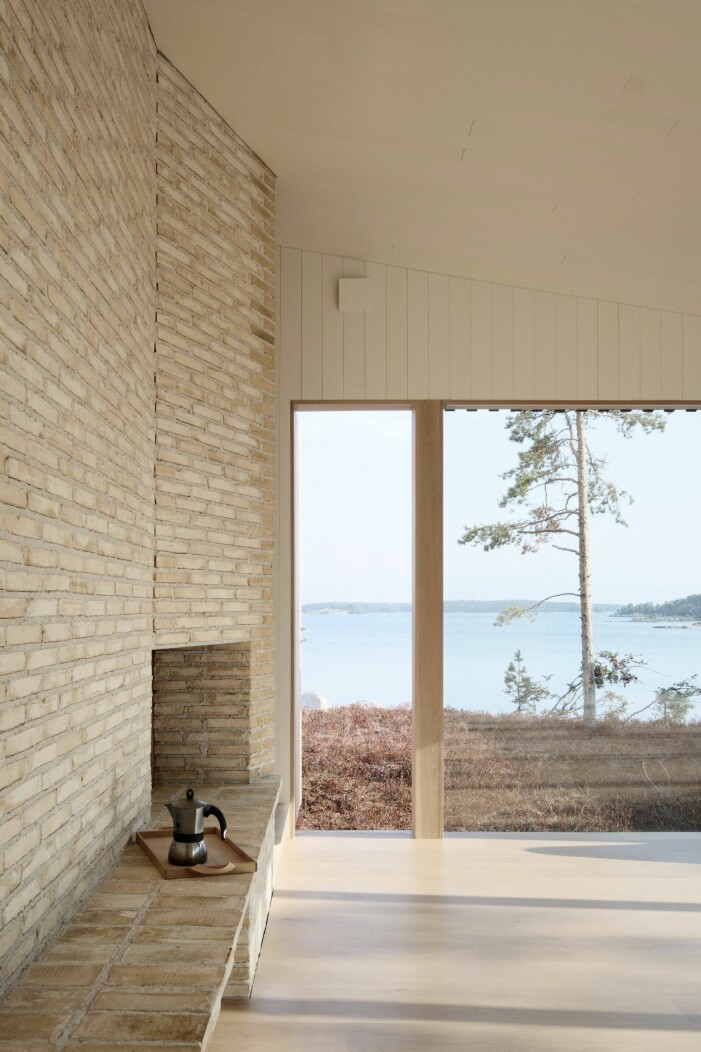 Vardagsrummet. Den teglade väggen med sin öppna spis vikarierar som bänk. Vardagsrum i studentritade huset Villa Furuholmen.