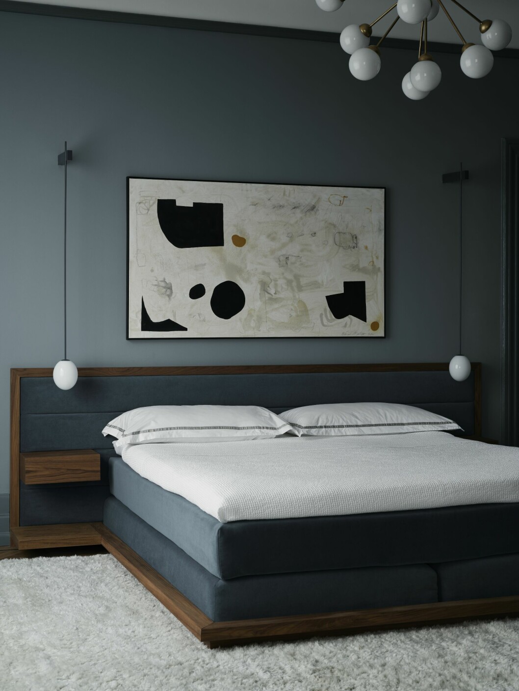 En sänggavel har designats i teak och mörkblå sammet. Även bäddmadrasserna har klätts in i samma sammetstyg. Sänglamporna The Philosophical egg av Michael Anastassiades och konstverket är av William McLure.