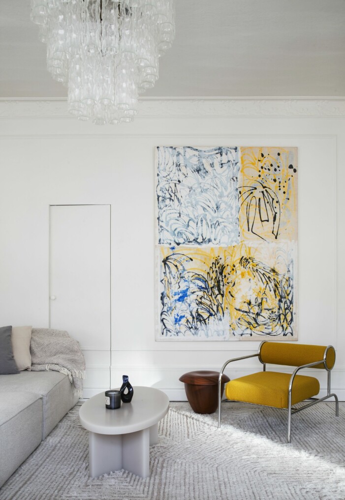 Bakom den lilla dörren döljer sig en garderob. Soffa, Bolia, soffbord av Caroline Sandström Blasiak i konstharts, fåtölj, Shiro Kuramata för Cappellini. Matta från Knut mattor, som Charlie designat tillsammans med Knut. Den stora tavlan har Jim Thorell målat med tusch, akryl och olja. Vardagsrum.