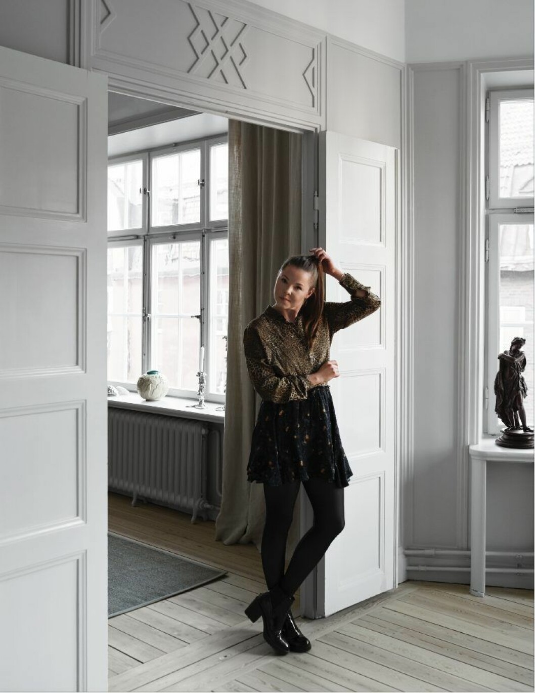 Madeleine står mellan kök och vardagsrum. Den eleganta färgen på alla väggar heter Skimming stone av Farrow and Ball. Skulpturen i fönstret är arvegods från Madeleines morfar och mormor. Hemma hos Madeleine Asplund Klingstedt. Den eleganta färgen på alla väggar heter Skimming stone av Farrow and Ball.