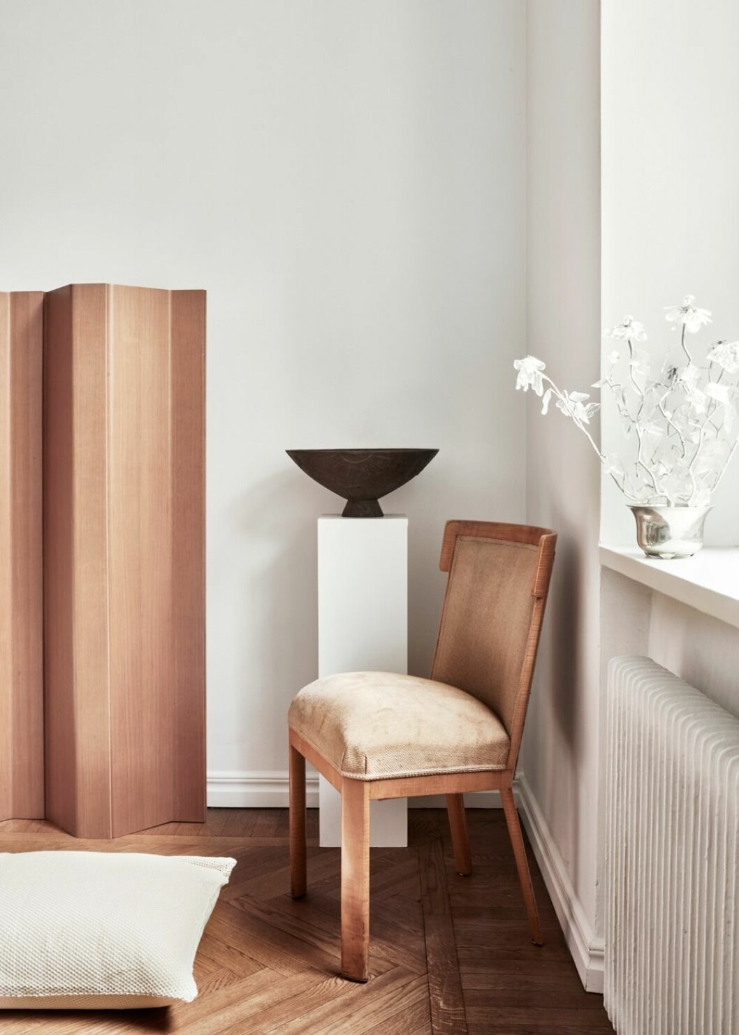 Örngott från Magniberg, Sex, i offwhite bomullsmesh. Stol, 30-tal, Carl Bergsten för Nordiska kompaniet. I fönstret står en kristallblomma från Svenskt tenn. Urnan på piedestalen designades på 20-talet av Olof Hult för Näfveqvarns bruk. 70-talsskärmen är av Poul Kjærholm för PP-möbler.