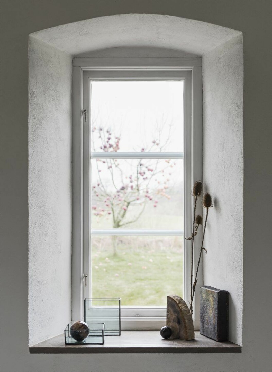 Tomtens enda äppelträd ger frukt från tidig till sen höst eftersom två sorter ympats in. I den djupa fönsternischen finns displaykuber i glas och prydnadssfärer i förstelnat trä, båda Typeo.se. Konstverk, Eva Wittbjer.