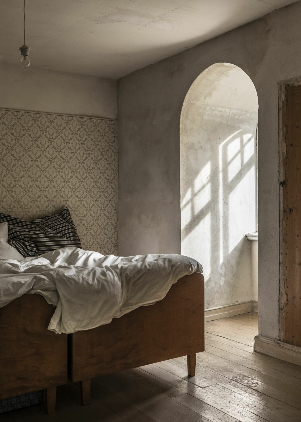 Ett av de fyra sovrummen på ovanvåningen. De tjocka väggarna gör att man sover lika rofyllt som i ett kloster. Väggarna är omputsade, men de gamla tapeterna är bevarade på en av väggarna. Sovrum i huset med äkta patina på Österlen.