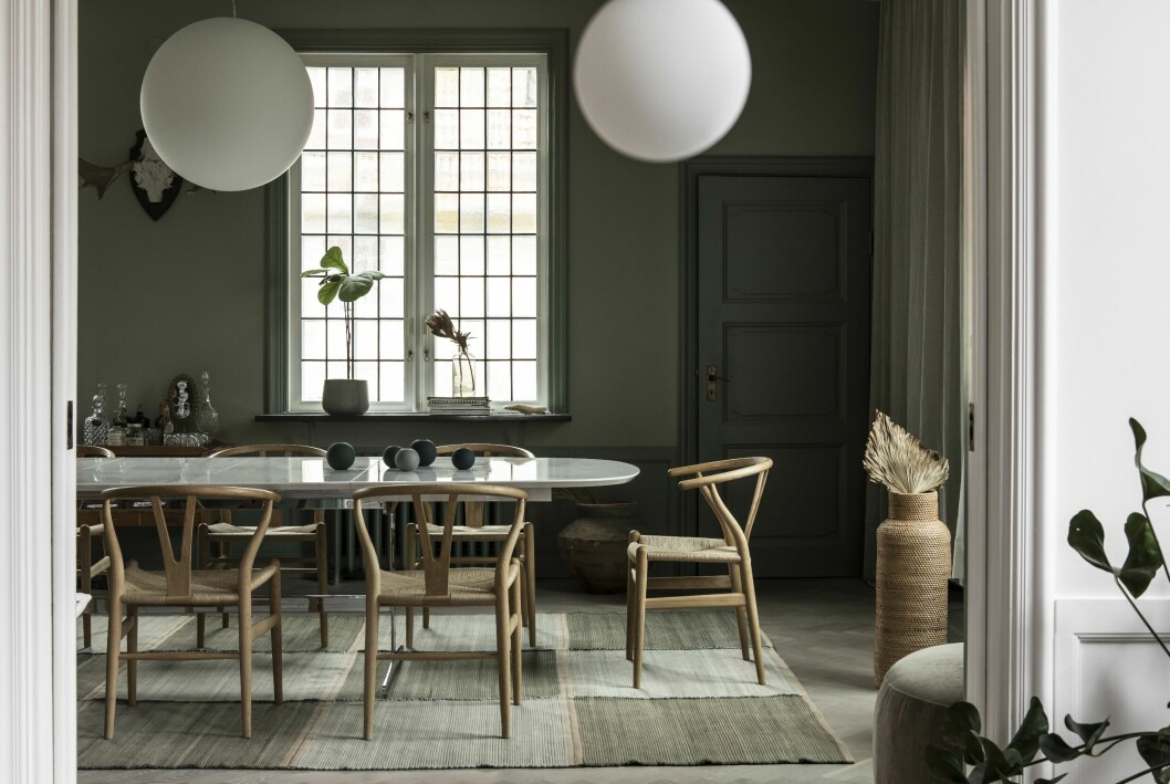 Vardagsrum med mötesplats vid stora bordet. Globlampor från Design house Sthlm. Vas i rotting samt palmblad från The straw. Y-stolar av Hans J Wegner. Modulmatta från Swedish rags. Gardiner från Gotain.