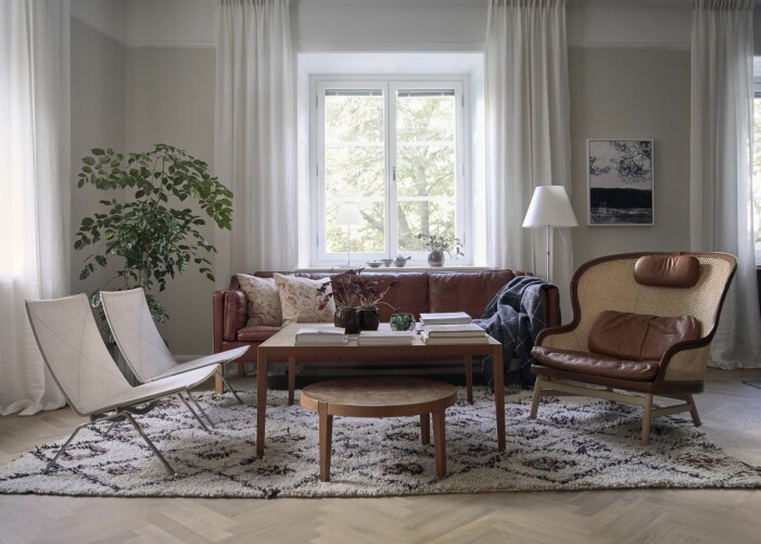 Träden utanför fönstren skapar ett vackert ljus i vardagsrummet. Ryamatta, Marrakech design. Fåtöljerna till vänster om soffbordet är PK 22 av Poul Kjærholm, de har liksom den konjaksfärgade soffan av Børge Mogensen, fått hänga med genom åren. Fåtöljen Dandy av Pierre Sindre för Gärsnäs. Golvlampa Costanza, Luceplan. Möbelskatt hemma hos ägarna av företaget Gärsnäs