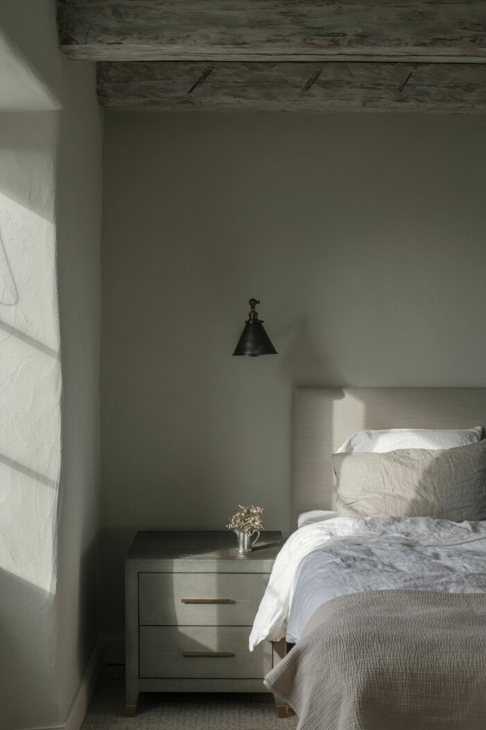 Sovrummen är lite mörkare än resten av huset för att inte bli för varma och ljusa under de långa sommarnätterna. Den rustika känslan från undervåningen går igen i linnetygerna och vägglampan i smidesjärn. Mörkt sovrum.