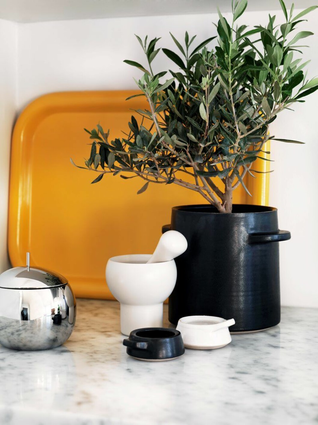 Svart keramikkruka och saltkar av keramikern Anna Gäfvert. Gul bricka av Ettore Sottsass, inköpt på Moma i New York. Morteln Aroma av Eero Aarnio, rostfri burk Fruit Basket av Sanaa från Alessi. mortel porslin