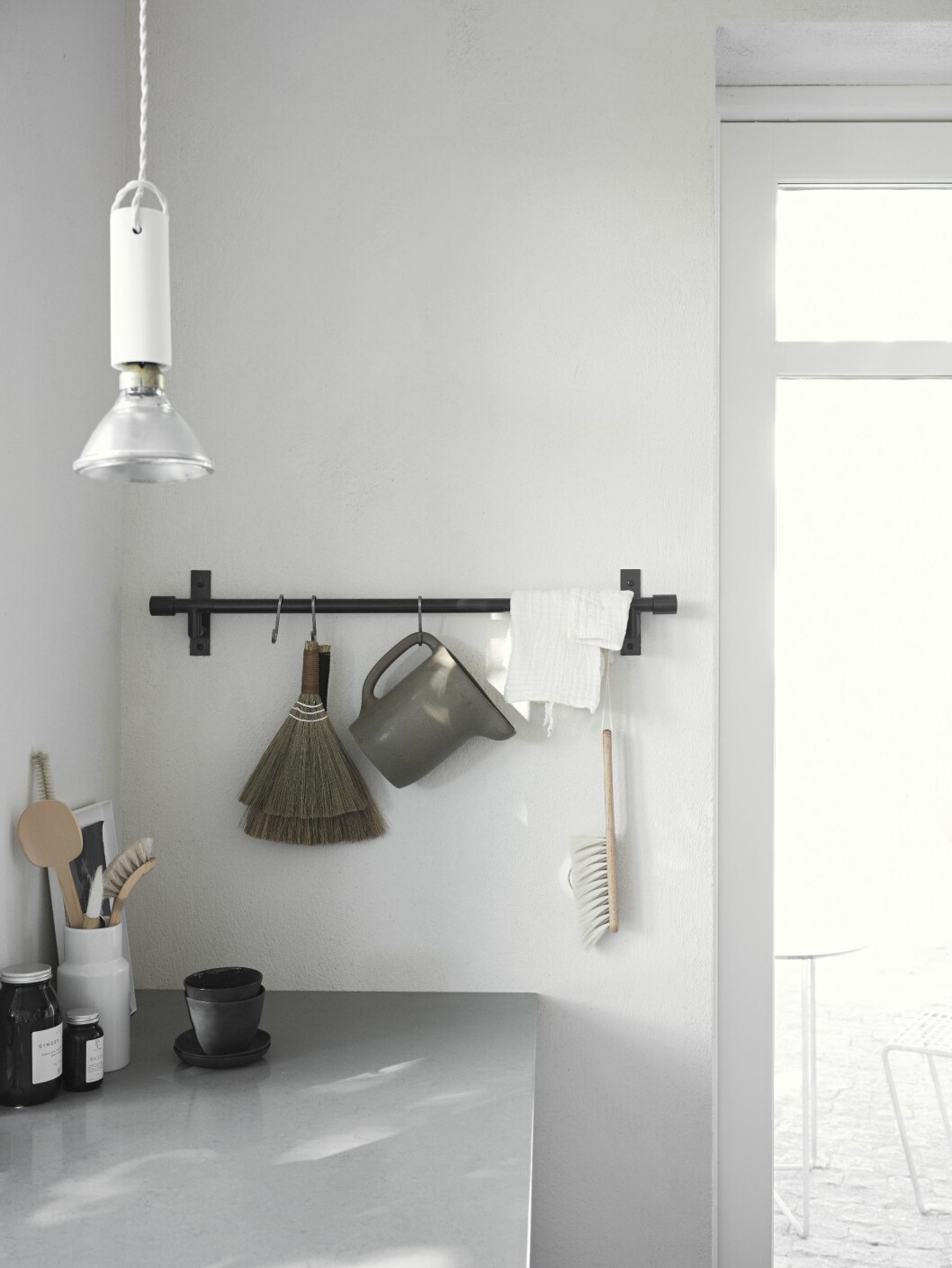 Diverse vardagsobjekt och rekvisita bildar blickfång på köksrelingen. Bänkskiva, Silestone Cygnus. Arbetsbelysning i keramiksockel Tied lamp från Menu. Köksreling med vardagsobjekt.