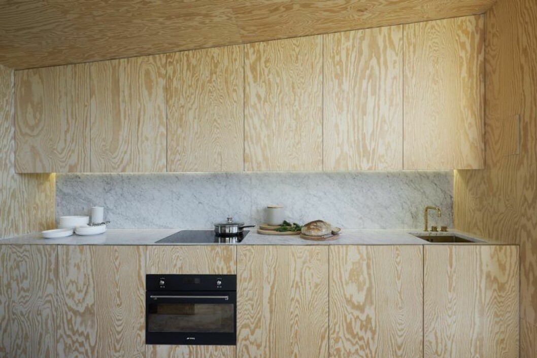 Kök med luckor av kvistfri furuplywood. En slits av carraramarmor från vägg till vägg utgör stänkskydd och diskbänk. Svart ugn från Smeg och blandare från Vola i obehandlad mässing, porslin Inwhite, Nordiska galleriet. Sommarhus Andreas Martin-Löf