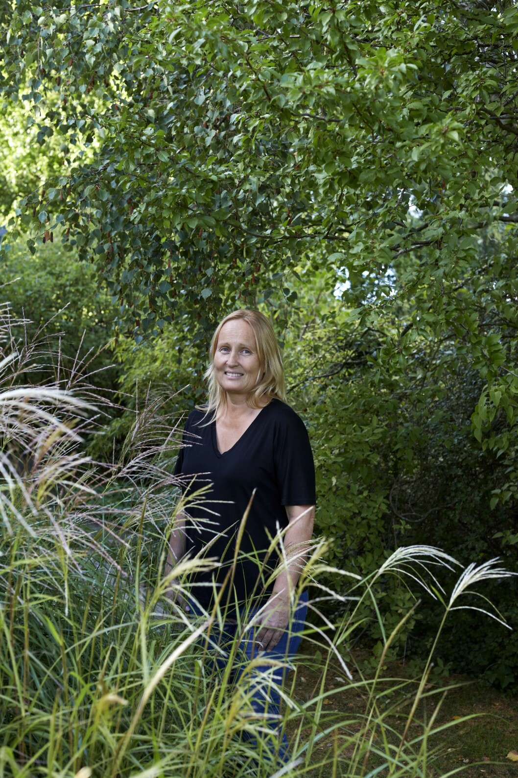 Susann i sin vildvuxna trädgård bakom svajande gräs. Foto: Sara Medina Lind Susann Larsson i sin trädgård i Lomma.