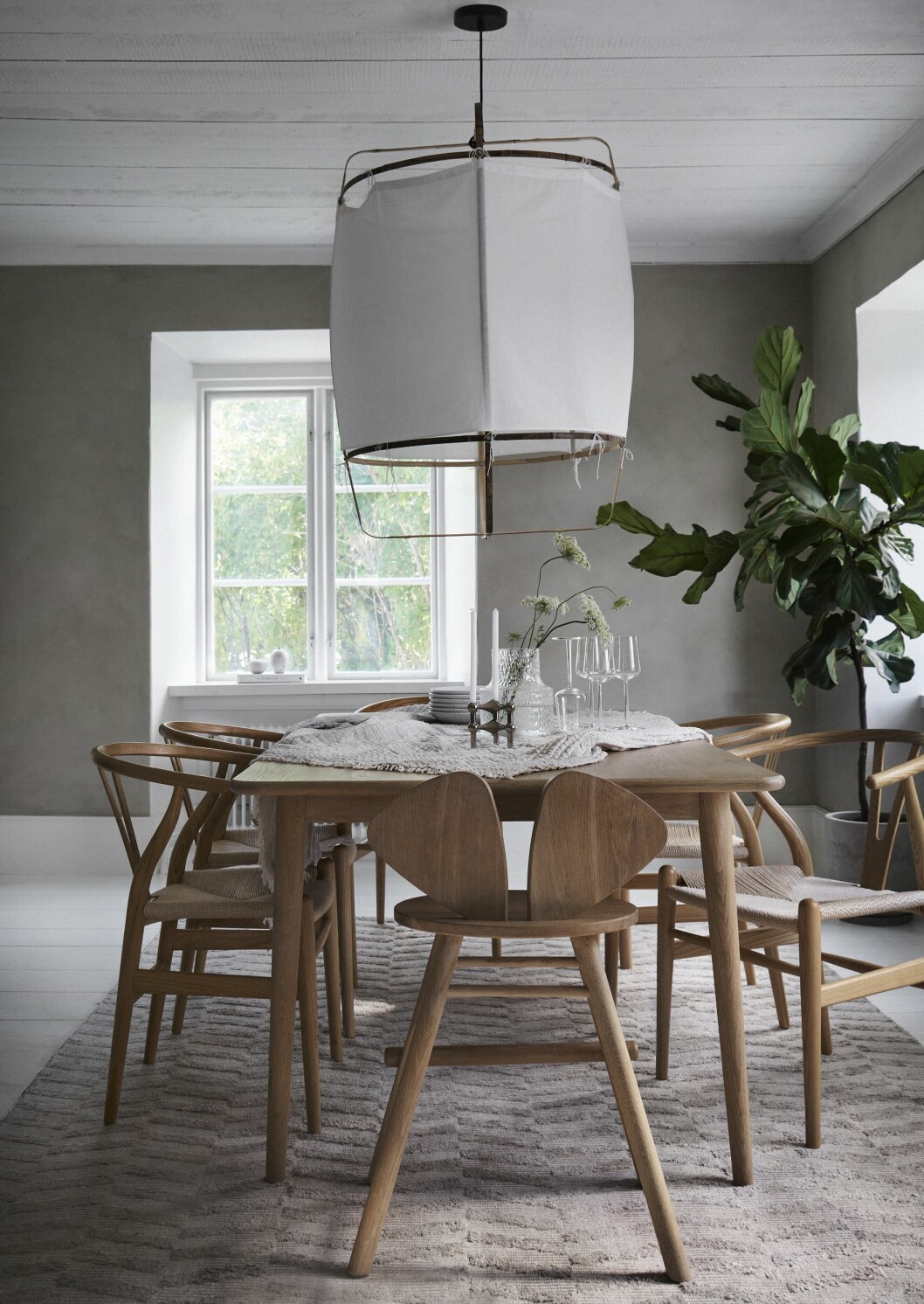 Tre fönster släpper in ljus i matrummet. Barnstol från Solhem Inredning. Bordet från EM Home passade till y-stolarna CH24. Pläd, Garbo & Friends. Glas från Iittala. Ljusstake, Stoff Nagel. Vas Kolonn, Skrufs glasbruk. Matta Chevron Lampa, Artilleriet. Matta Chevron Aluminium, Classic Collection. I fönstret står vaser från G.A.D. Kök med grå väggkulör.