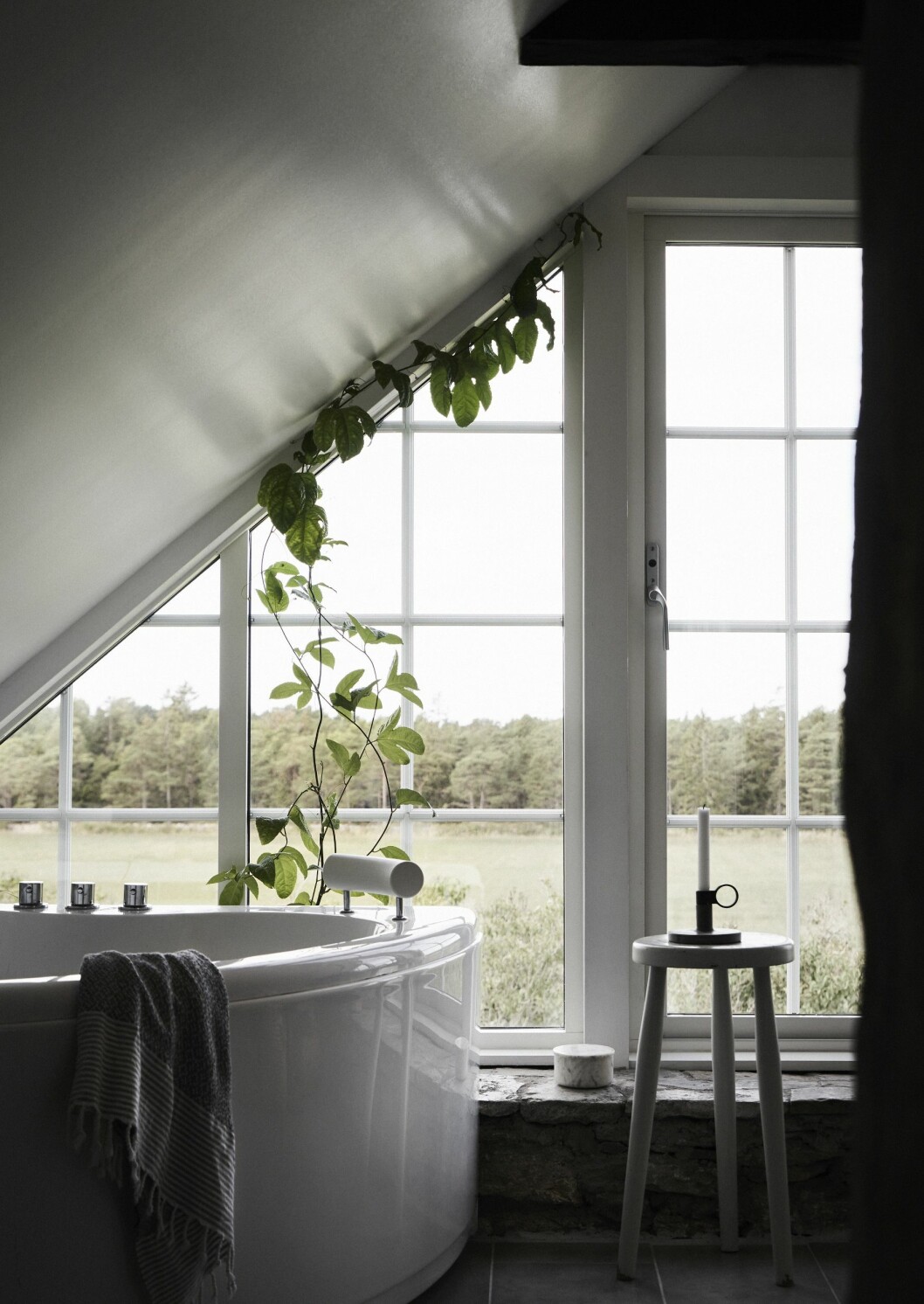 På gaveln som vetter mot havet tog Linda och Martin bort en tillbyggnad, satte in ett glasparti och gjorde det till badrum. Härifrån har familjen utsikt över solens nedgång i havet intill Karlsöarna. När syrenhäcken nedanför blommar fyller den rummet med doft. Växten är en passionsfrukt från Lilla Bjers. Marmorburk köpt på Lotta Agatons inredningsbutik. Antik pall från Akantus Visby. Ljusstake, Design by Kibisi. Gaveln vetter mot havet.