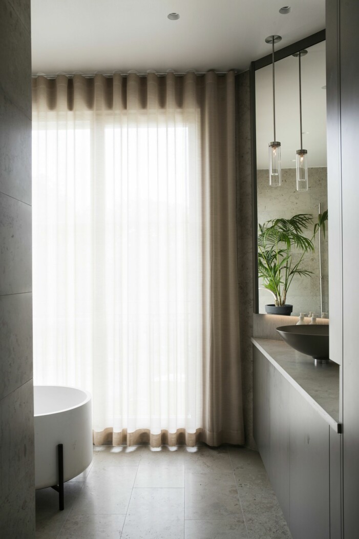 Badrum med morgonsol. Möblerna är ritade av Olle Rex och Jimmy Källqvist och producerade av Nacka snickerier. Badkar från Norm architects. Lampor från John Cullen och handfat från Agape. På golvet <span class=" italic" data-lab-italic_desktop="italic">Norrvangekalksten</span> från Slite stenhuggeri. Skira bruna gardiner