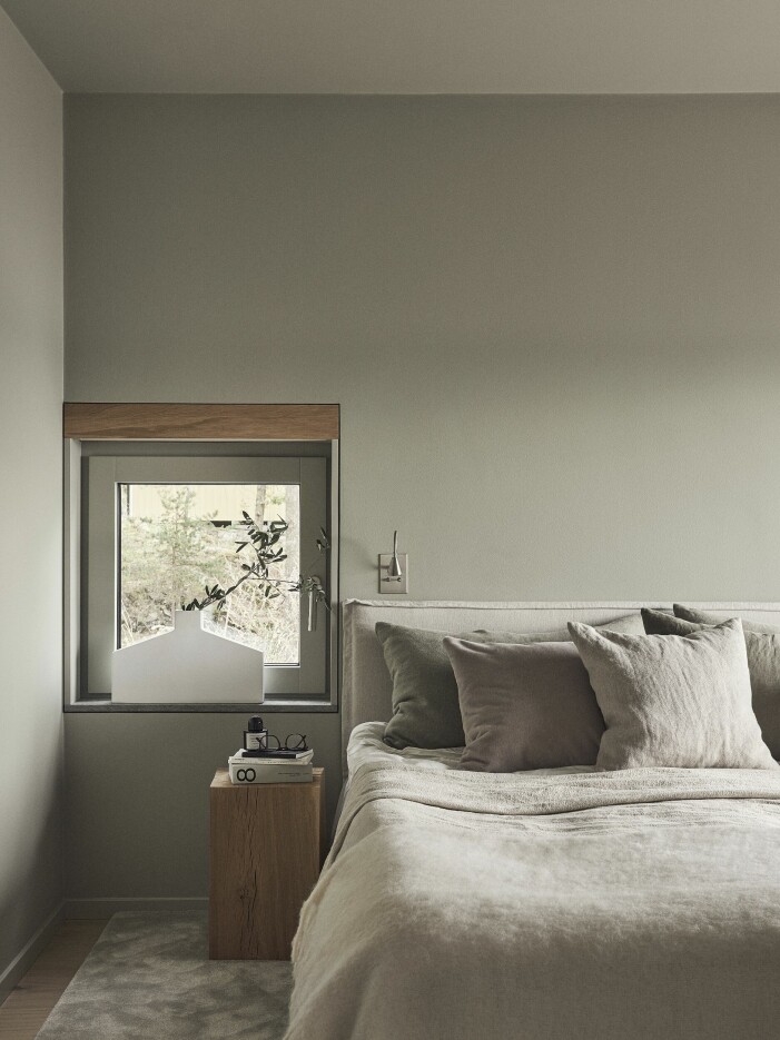 Sängkläder, Ogland. Vas i fönstret från Kose Milano. Sänggavel ritad av Lotta Agaton interiors och klädd i linnetyg från Astrid. Kuddar i grönt och beige linnetyg från Astrid. Sängbord, specialtillverkat ekpodium. Läslampa, Tulipe från Meljac. Sovrum med ljusa sängkläder.