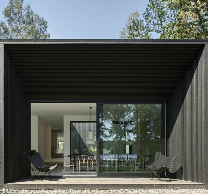 Mitt i huset bakom matbordet skymtar en 30 kvadratmeter stor atriumgård som adderar grönska till den minimalistiska interiören. Fladdermusfåtöljer från Cuero design. Uteplats med stora fönster in i huset.
