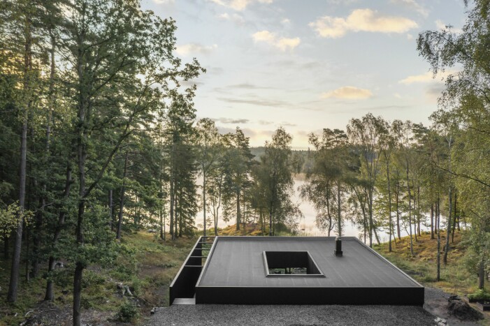 Det till hälften nedgrävda huset, här sett från vändplanen, har en stomme i lättbetong som klätts i en granfasad. Vacker utsikt över vatten och skogslandskap.